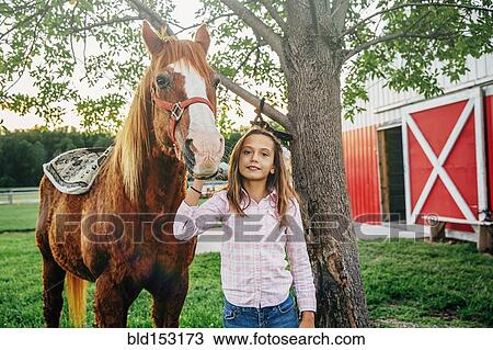 Stock Image - Caucasian girl walking horse outside barn on farm. Fotosearch