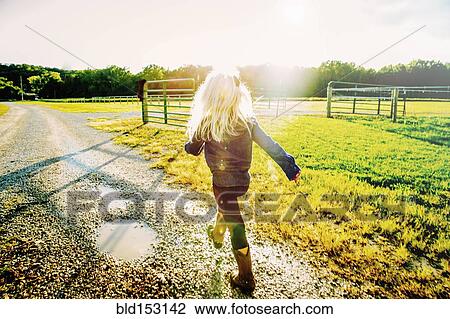 Stock Image - Caucasian girl walking on dirt road on ranch. Fotosearch