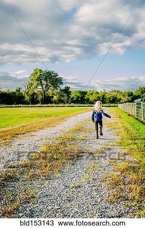 Stock Image - Caucasian girl walking on dirt road on ranch. Fotosearch