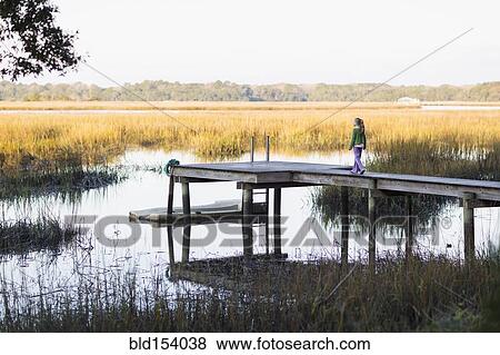 Stock Photo - Caucasian girl walking on wooden dock in lake. Fotosearch