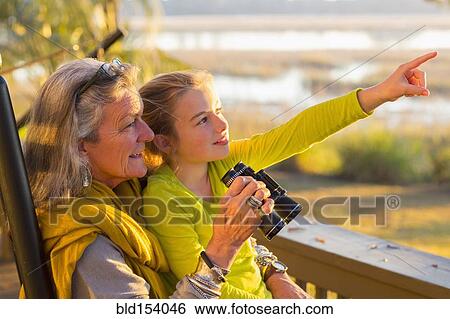 Stock Photograph - Caucasian grandmother and granddaughter using binoculars on porch. Fotosearch