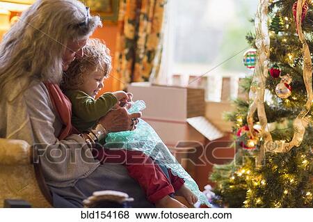 Stock Photo - Caucasian grandmother and grandson opening presents near Christmas tree. Fotosearch
