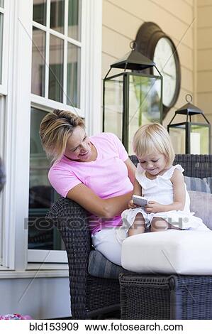 Stock Photo - Caucasian mother and daughter using cell phone on porch. Fotosearch