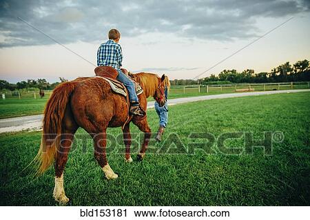 Stock Image - Caucasian mother and son walking horse on ranch. Fotosearch