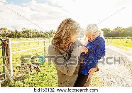 Stock Image - Caucasian mother tickling daughter on rural road. Fotosearch