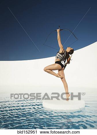 Stock Image - Caucasian woman aiming bow and arrow on ice floe. Fotosearch