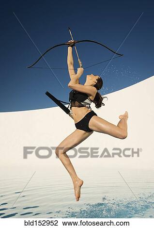 Stock Image - Caucasian woman aiming bow and arrow. Fotosearch