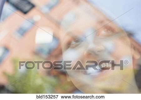 Stock Photo - Caucasian woman and reflection of apartment buildings in window. Fotosearch