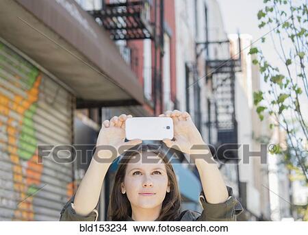 Caucasian woman taking cell phone photograph on urban sidewalk View Large Photo Image Picture - Caucasian woman taking cell phone photograph on urban sidewalk. Fotosearch