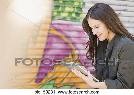 Stock Image - Caucasian woman using digital tablet near graffiti wall. Fotosearch