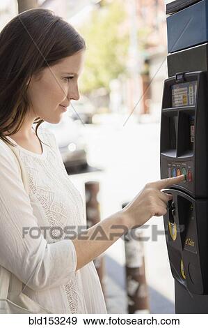 Stock Photo - Caucasian woman using parking meter on urban sidewalk. Fotosearch