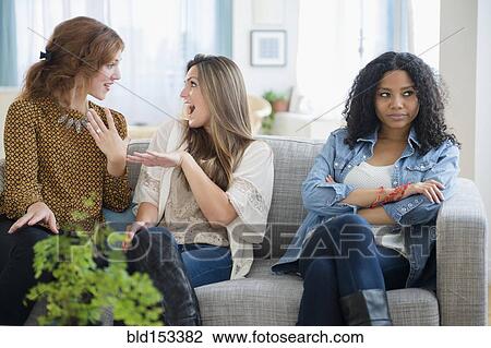 Stock Image - Chatting women ignoring upset friend on sofa. Fotosearch