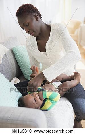 Stock Image - Close up of Black mother changing diaper of baby boy. Fotosearch