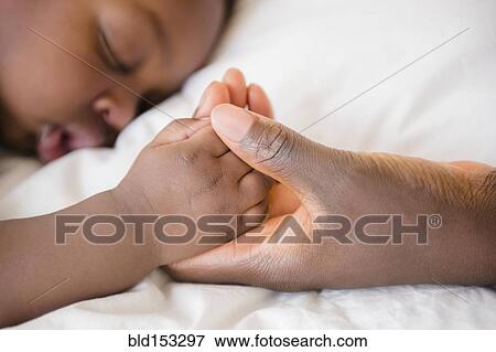 Close up of Black mother holding hand of sleeping baby View Large Photo Image Stock Photo - Close up of Black mother holding hand of sleeping baby. Fotosearch