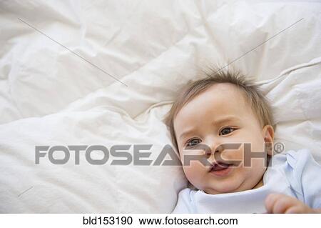 Stock Image - Close up of mixed race baby laying on bed. Fotosearch