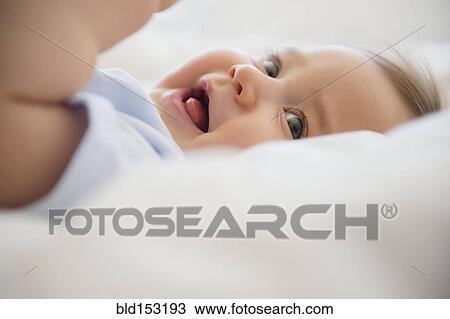 Stock Image - Close up of mixed race baby laying on bed. Fotosearch