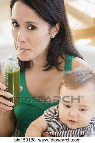 Close up of mixed race mother holding baby and drinking green juice View Large Photo Image Stock Photo - Close up of mixed race mother holding baby and drinking green juice. Fotosearch