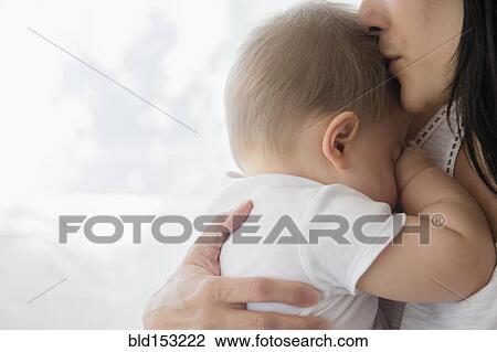 Stock Image - Close up of mixed race mother kissing baby on forehead. Fotosearch