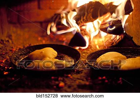 Stock Photo - Close up of pastries cooking in skillets near wood fire. Fotosearch
