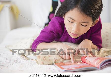 Stock Image - Close up of Vietnamese girl reading book on bed. Fotosearch