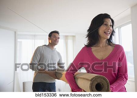 Stock Photograph - Couple carrying roll of carpet in living room. Fotosearch