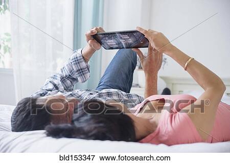 Stock Photo - Couple using digital tablet and laying on bed. Fotosearch