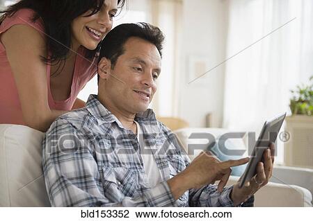 Couple using digital tablet on sofa in living room View Large Photo Image Stock Image - Couple using digital tablet on sofa in living room. Fotosearch