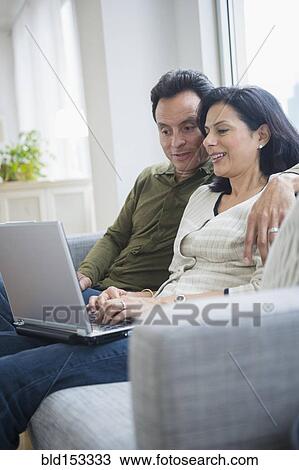 Couple using laptop on sofa in living room View Large Photo Image Stock Image - Couple using laptop on sofa in living room. Fotosearch