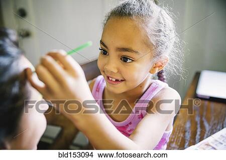 Girl painting face of mother at kitchen table View Large Photo Image Picture - Girl painting face of mother at kitchen table. Fotosearch