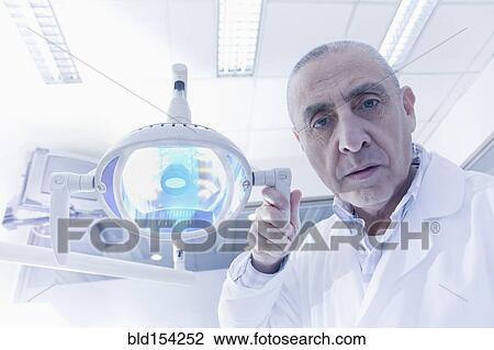 Hispanic dentist holding lamp in office View Large Photo Image Stock Image - Hispanic dentist holding lamp in office. Fotosearch