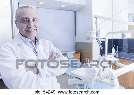 Stock Photo - Hispanic dentist smiling near chair in office. Fotosearch