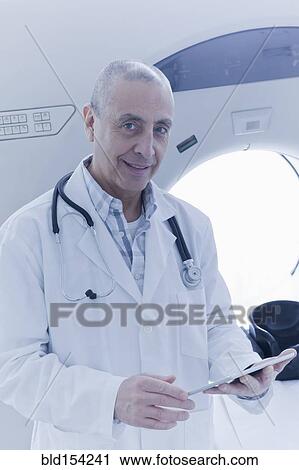 Stock Image - Hispanic doctor using digital tablet near MRI scanner. Fotosearch
