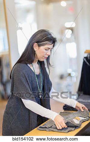 Hispanic small business owner folding clothes in store View Large Photo Image Stock Image - Hispanic small business owner folding clothes in store. Fotosearch