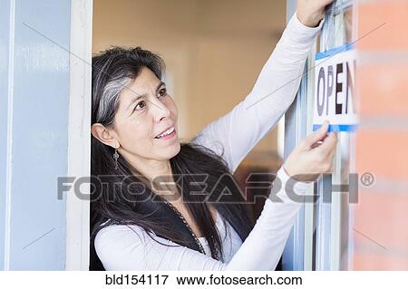 Stock Photo - Hispanic small business owner hanging open sign on door. Fotosearch