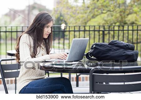 Stock Image - Hispanic woman using laptop at table outdoors. Fotosearch
