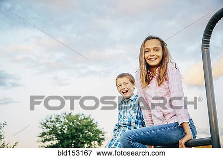 Stock Photo - Low angle view of Caucasian children sitting outdoors. Fotosearch