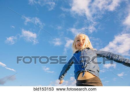 Low angle view of Caucasian girl standing under blue sky View Large Photo Image Stock Image - Low angle view of Caucasian girl standing under blue sky. Fotosearch