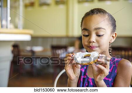 Stock Image - Mixed race girl eating bagel in cafe. Fotosearch