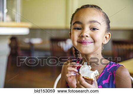 Mixed race girl eating bagel in cafe View Large Photo Image Stock Photo - Mixed race girl eating bagel in cafe. Fotosearch