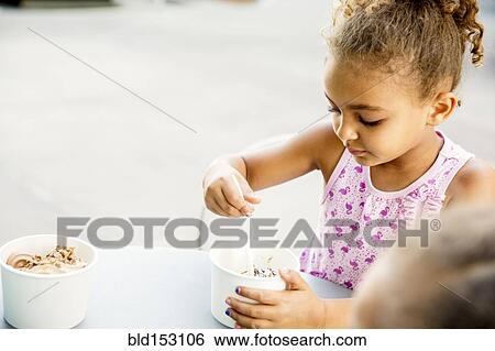 Stock Photograph - Mixed race girl eating ice cream at outdoor cafe. Fotosearch