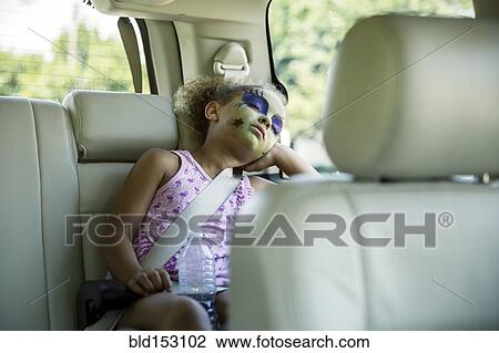 Stock Image - Mixed race girl in face paint sleeping in car back seat. Fotosearch