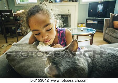 Mixed race girl playing with pet cat on sofa View Large Photo Image Stock Image - Mixed race girl playing with pet cat on sofa. Fotosearch