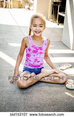 Stock Photo - Mixed race girl sitting with legs crossed on sidewalk. Fotosearch