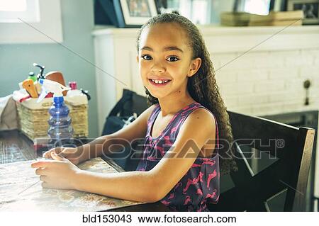 Stock Image - Mixed race girl smiling at kitchen table. Fotosearch