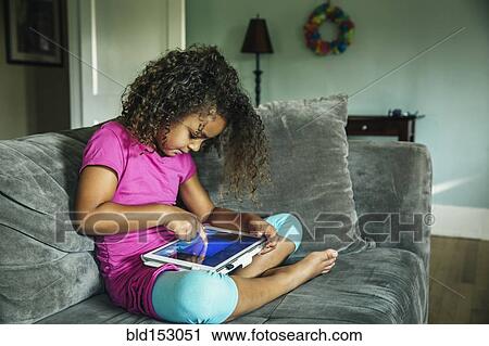Stock Image - Mixed race girl using digital tablet on sofa. Fotosearch