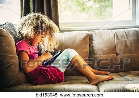 Mixed race girl using digital tablet on sofa View Large Photo Image Stock Photography - Mixed race girl using digital tablet on sofa. Fotosearch