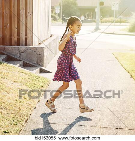 Stock Photography - Mixed race girl walking on neighborhood sidewalk. Fotosearch