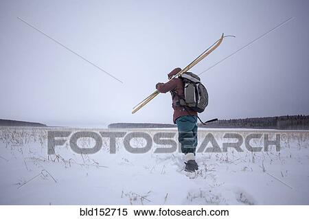 Stock Photography - Mixed race man carrying skis in snowy field. Fotosearch