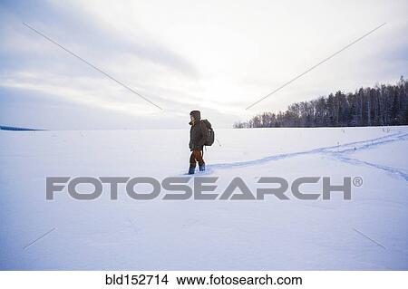 Picture - Mixed race man walking in snowy field. Fotosearch