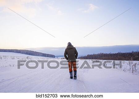 Stock Image - Mixed race man walking in snowy field. Fotosearch